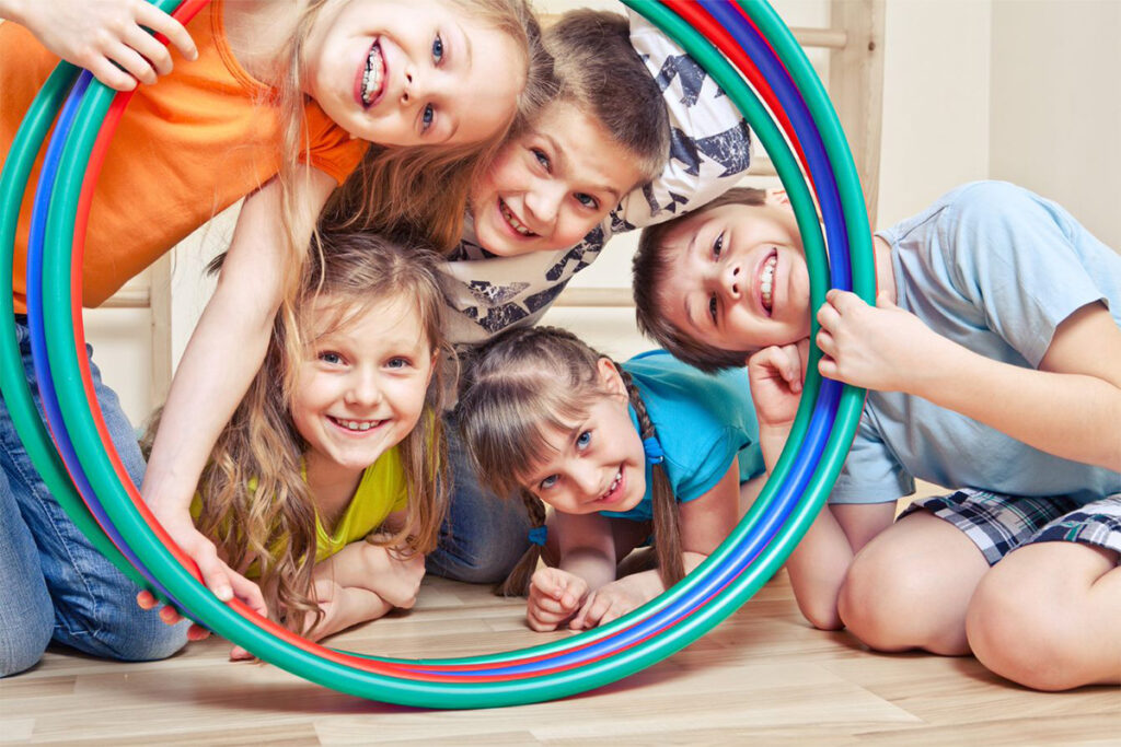 Five Kids sticking their heads behind several hula hoops and smiling